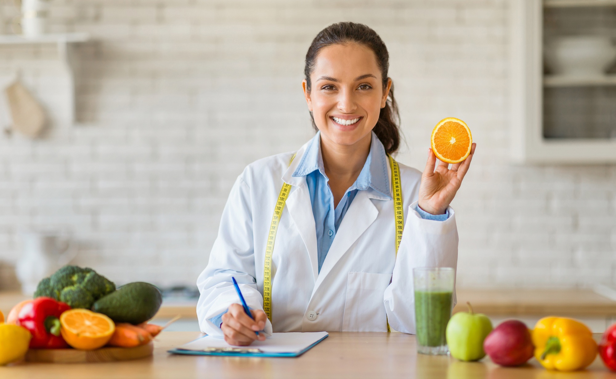 Dietician with orange in kitchen, writing nutrition plan